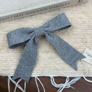 Gros plan d'une pince à cheveux nœud en tricot gris posée sur un fond beige texturé