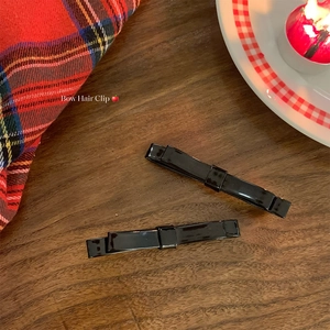 Close-up of two black glossy bow hair clips on a wooden surface with a festive setup