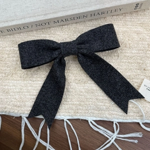 Détail du nœud papillon en laine gris foncé sur un fond de tapis texturé et minimaliste