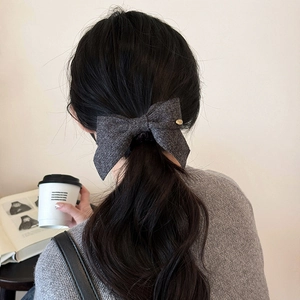 Elegant dark grey wool bow hair tie with a gold charm shown on a low ponytail