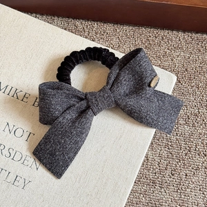 Close-up of grey bow scrunchie with fine texture and elegant gold oval metal tag