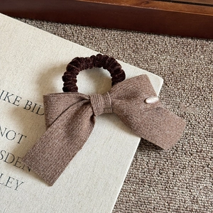 Close-up of a brown knit bow hair scrunchie with a gold metal tag on soft books