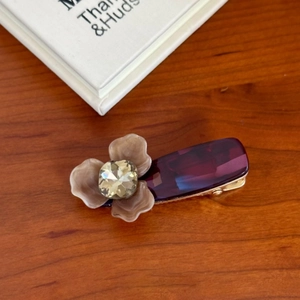 Dettaglio del fermaglio viola con fiore testurizzato e grande gemma dorata lucida