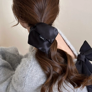 Détail d'un chouchou en satin de soie noir avec étiquette Hand Made sur les cheveux