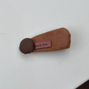 Detail einer braunen Strick-Haarklammer mit Stoffknopf und sweet love Lederetikett
