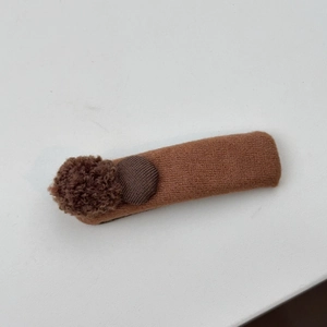 Detailansicht der kaffeebraunen Strick-Haarspange mit Plüschball und rundem Knopf-Dekor