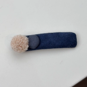 Nahaufnahme einer Winter-Haarklammer aus blauem Strick mit beigefarbenem Bommel-Detail