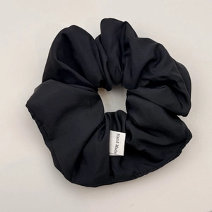 Detailed close-up of handmade black ruched scrunchie with satin texture and tag