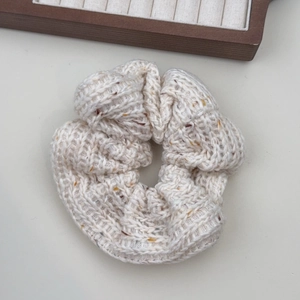 Gros plan d'un chouchou en maille crème avec des taches colorées et texture tissée