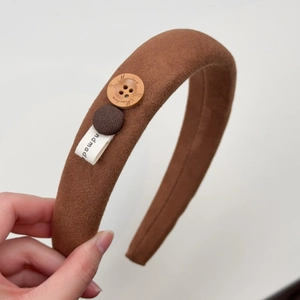 Detail eines kaffeebraunen Samt-Haarreifens mit Holzknopf und handgemachtem Etikett