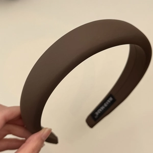 Detail view of a thick padded dark brown headband featuring a handmade brand label