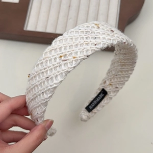 Détail d'un bandeau en tricot blanc crème fait main avec des mouchetures colorées et étiquette