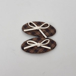 Detail view of plaid fabric hair clips in brown and black with small white bow accents
