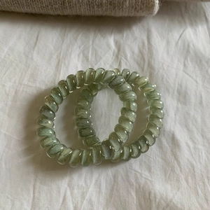 Detail of two translucent olive green spiral telephone wire hair ties on white fabric