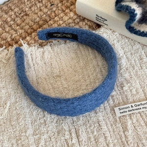 Close-up of blue textured knitted headband with Hand Made label on beige fabric