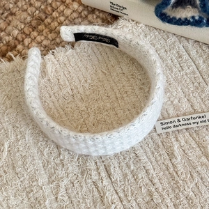 Detailed close-up of cream knit headband with Hand Made label on textured background