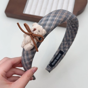 Detail of grey plaid headband with plush bear and coffee bow tie in soft lighting