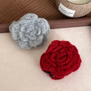 Handcrafted crochet rose hair clips in grey and red yarn on a rustic wooden tray