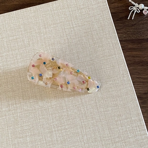 Detail showing marble texture resin hair clip with colorful rhinestones on beige fabric