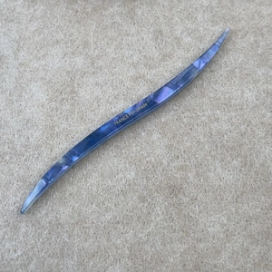 Dettaglio della forcina in acetato blu marmorizzato curvo con scritte dorate fatte a mano