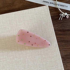 Close-up of pink triangular hair clip with colorful rhinestones on a decorative card