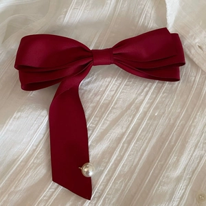 Détail d'un nœud en satin bordeaux avec une perle blanche élégante sur le ruban long