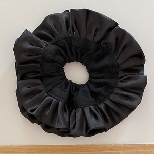 Dettaglio di un grande elastico scrunchie in raso nero con pieghe morbide e finitura lucida