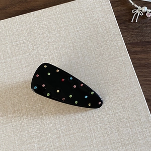 Close-up of black geometric hair clip with colorful scattered rhinestones and glossy finish