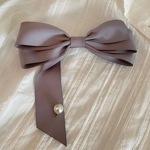 Détail d'une pince à cheveux nœud en satin rose poudré avec une perle élégante pendante