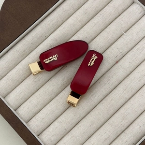 Close-up of two deep red acetate hair clips with gold metal base and French text engraving