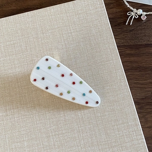 Close-up of white resin hair clip with colorful rhinestones on beige fabric background