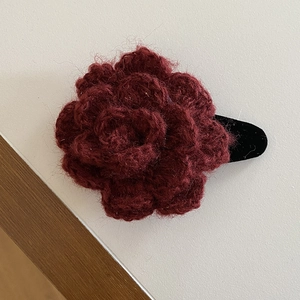 Detailed close-up of handmade red crochet rose hair clip with soft yarn texture