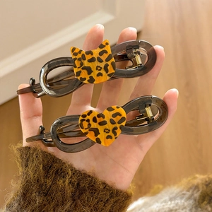 Handheld display of leopard print cat and heart-shaped hair clips in dark grey translucent plastic