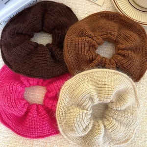 Oversized plush knitted scrunchies in four autumn colors on a soft textured background