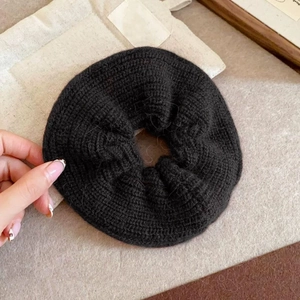 Macro detail of black knitted scrunchie showing thick yarn texture and soft pleats