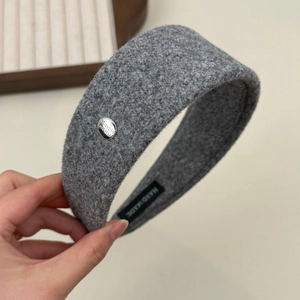 Detail of grey bouclé headband featuring an engraved silver metal tag and handmade label