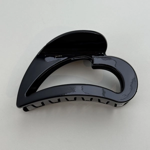 Close-up of a glossy black heart-shaped hair claw clip on a light textured surface