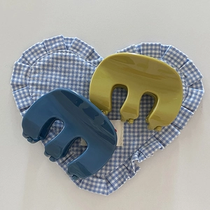 Minimalist M-shaped hair claws in navy blue and olive green on a checkered background