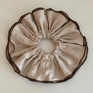 Détail d'un chouchou en satin champagne avec texture soie et bordure tissée marron