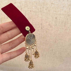 Detail of vintage golden ethnic earrings with bells and tassels on red velvet