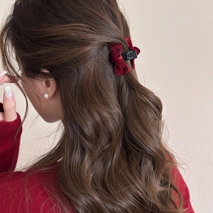 Detail of burgundy velvet bow hair claw clip styled on long wavy hair for women
