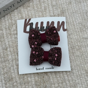Detail of two handmade red sequin bow hair clips on a white display card for girls