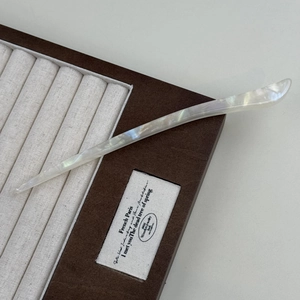 Elegant white acetate hair pin with pearlescent texture on a brown display case