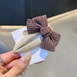 Hand holding a vintage brown corduroy bow hair clip on a beige fabric base display