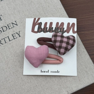 Dettaglio di due fermagli per capelli a forma di cuore in tessuto rosa e marrone plaid