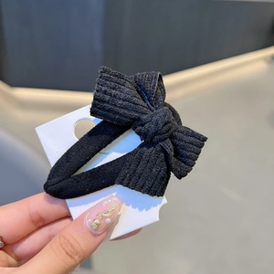 Close-up of black ribbed fabric bow hair clip on a display card held by hand