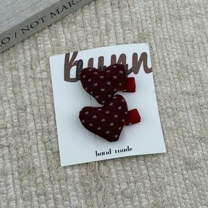 Pair of red heart-shaped fabric hair clips with white polka dots on a display card