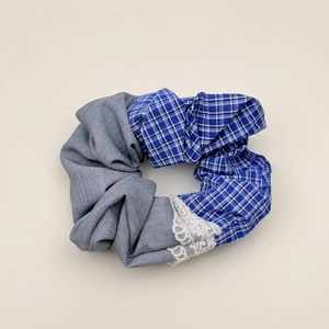 Detail of grey fabric and blue checkered pattern scrunchie with white lace trim