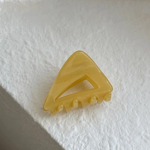 Macro detail of a bright yellow acetate triangular hair claw clip on stone background