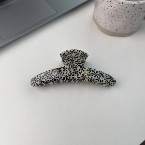 Grosse pince à cheveux crème avec motif à pois noirs posée sur un bureau blanc